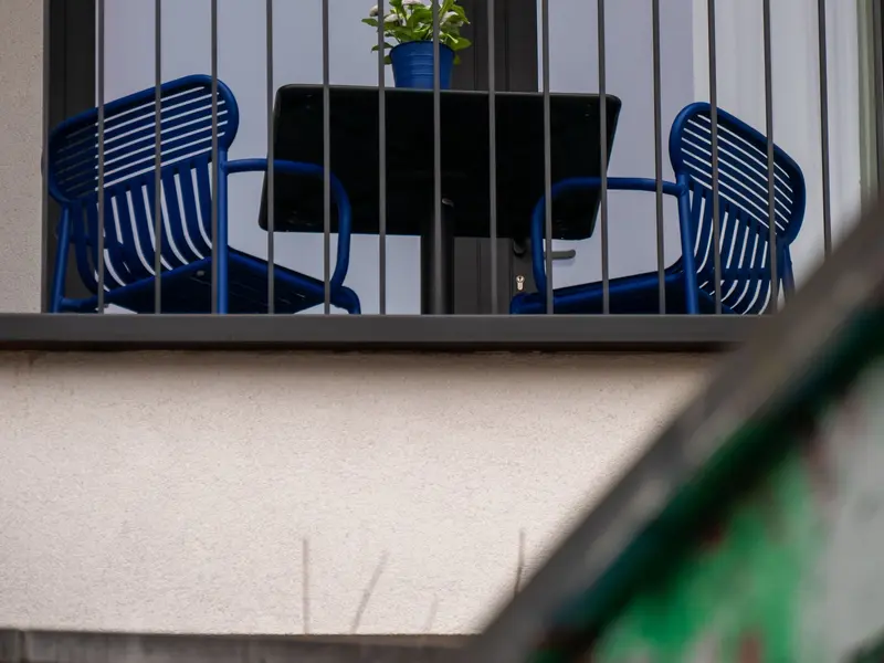 Balkon s tamnom metalnom ogradom, plavim stolicama i stolom